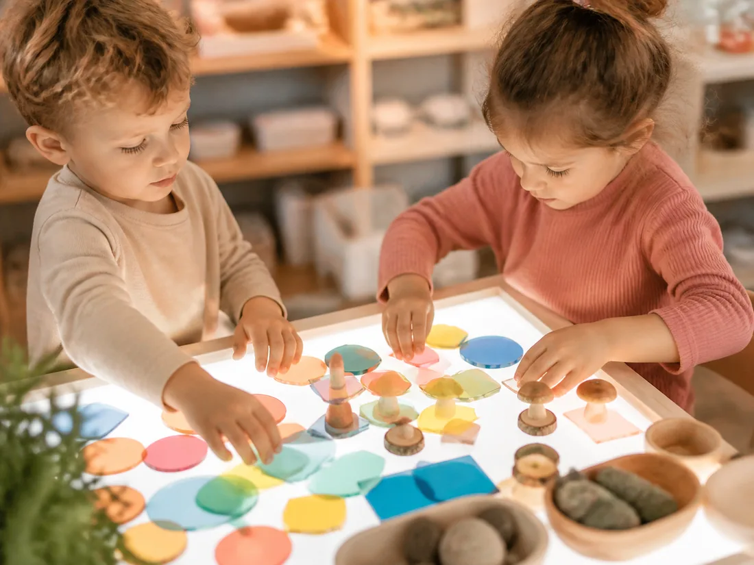 Dos niños exploran formas translúcidas y materiales naturales en una mesa de luz
